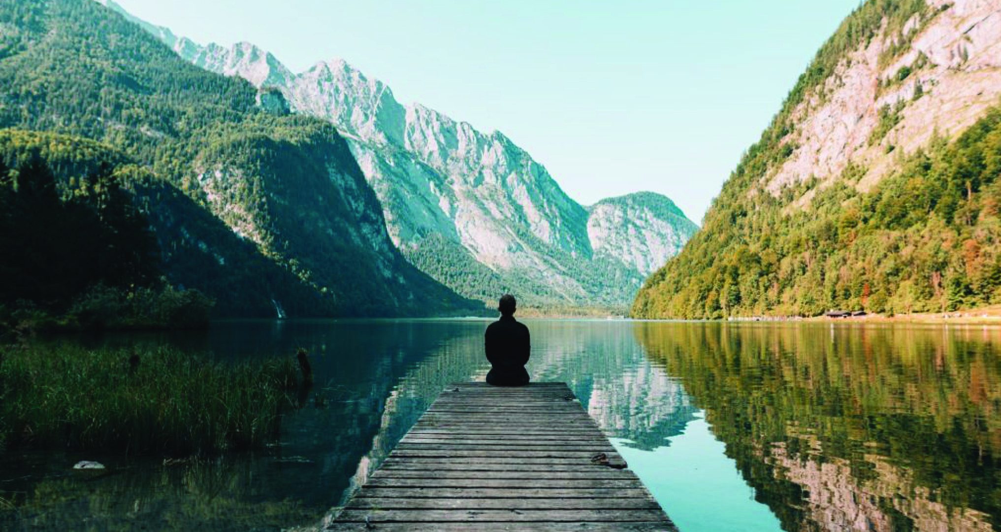 man sitting on dock looking at the mountains